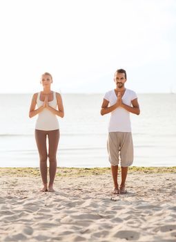 fitness, sport, friendship and lifestyle concept - couple making yoga exercises on beach