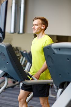 sport, fitness, lifestyle, technology and people concept - man with earphones exercising on treadmill in gym