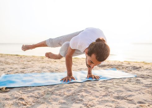 fitness, sport, people and lifestyle concept - man doing yoga exercises on mat outdoors