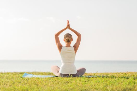 fitness, sport, people and lifestyle concept - of woman making yoga exercises on mat outdoors from back