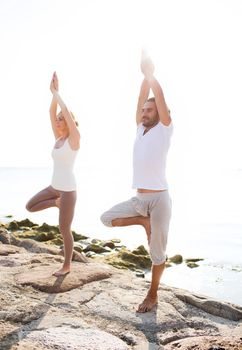 fitness, sport, friendship and lifestyle concept - couple making yoga exercises on beach
