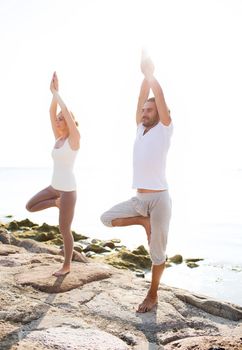 fitness, sport, friendship and lifestyle concept - couple making yoga exercises on beach