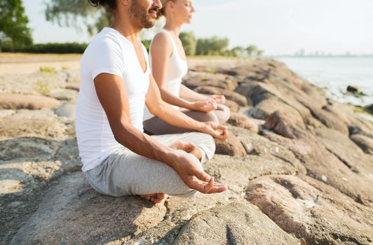 fitness, sport, people and lifestyle concept - close up of couple making yoga exercises sitting on pier outdoors