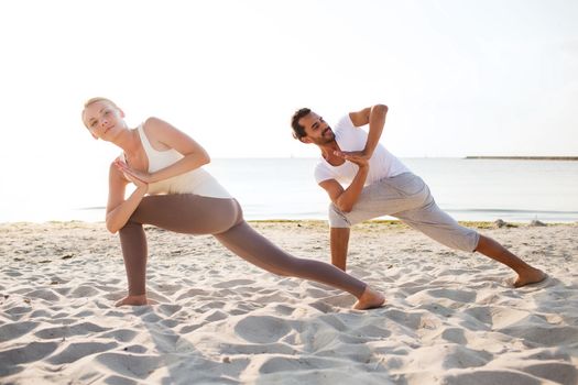 fitness, sport, friendship and lifestyle concept - couple making yoga exercises on beach