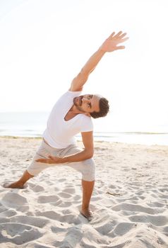 fitness, sport, people and lifestyle concept - smiling man making yoga exercises on beach