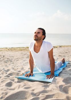 fitness, sport and lifestyle concept - man doing yoga exercises lying on mat outdoors