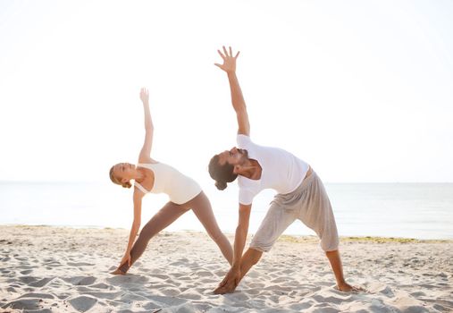 fitness, sport, friendship and lifestyle concept - couple making yoga exercises on beach