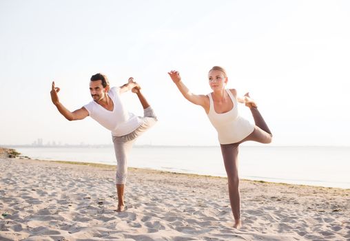 fitness, sport, friendship and lifestyle concept - couple making yoga exercises on beach