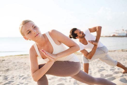 fitness, sport, friendship and lifestyle concept - close up of couple making yoga exercises on beach