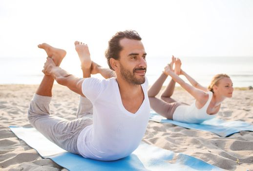 fitness, sport, friendship and lifestyle concept - couple making yoga exercises lying on mats outdoors