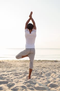 fitness, sport, people and lifestyle concept - man making yoga exercises on sand outdoors from back