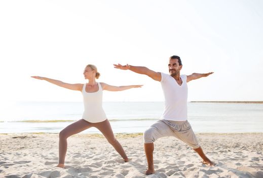 fitness, sport, friendship and lifestyle concept - couple making yoga exercises on beach