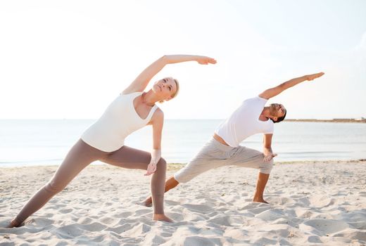 fitness, sport, friendship and lifestyle concept - couple making yoga exercises on beach