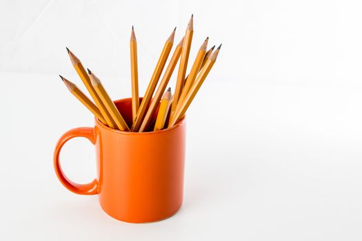 Orange mug with pencils on white background