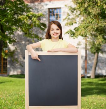 people, advertisement and education concept - happy little girl pointing finger to blackboard