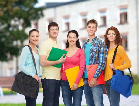 friendship, school, education and people concept - group of smiling teenagers with folders and school bags over campus background