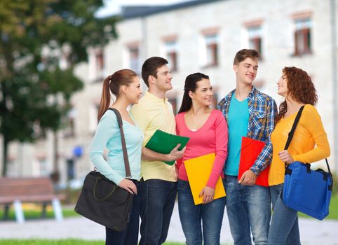 friendship, school, education and people concept - group of smiling teenagers with folders and school bags over campus background