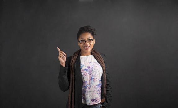 South African or African American black woman teacher or student with a good idea or answer standing against a chalk blackboard background inside