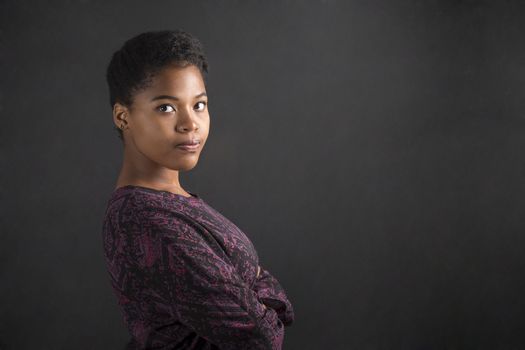 South African or African American woman teacher or student with arms folded on chalk black board background