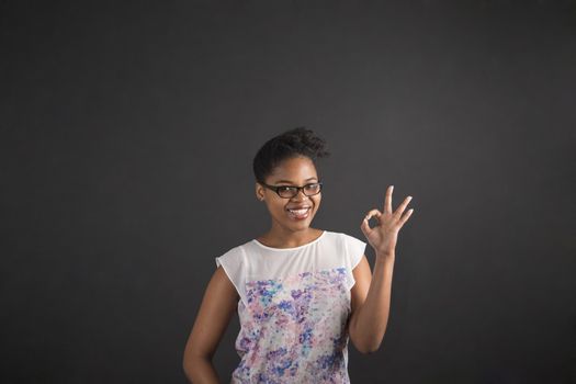 South African or African American black woman teacher or student holding up a perfect hand signal on a chalk blackboard background inside