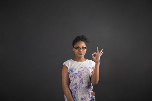 South African or African American black woman teacher or student holding up a perfect hand signal on a chalk blackboard background inside