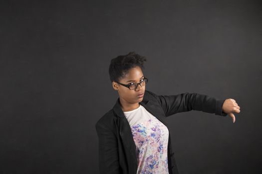 South African or African American black woman teacher or student with thumbs down hand signal on a chalk black board background inside