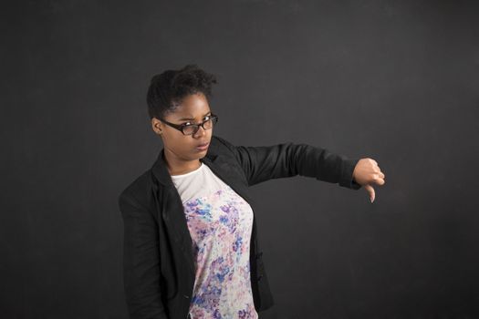 South African or African American black woman teacher or student with thumbs down hand signal on a chalk black board background inside