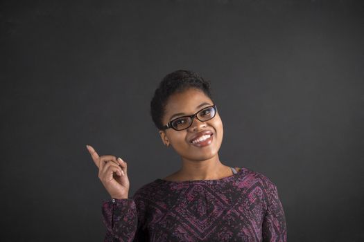 South African or African American black woman teacher or student with a good idea or answer standing against a chalk blackboard background inside