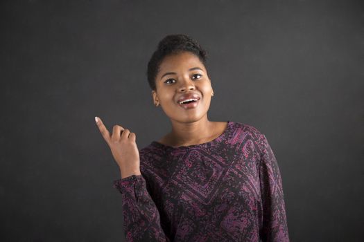 South African or African American black woman teacher or student with a good idea or answer standing against a chalk blackboard background inside