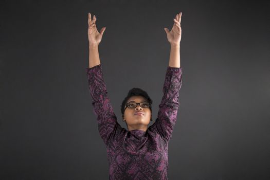 South African or African American woman teacher or student reaching for the sky on blackboard background