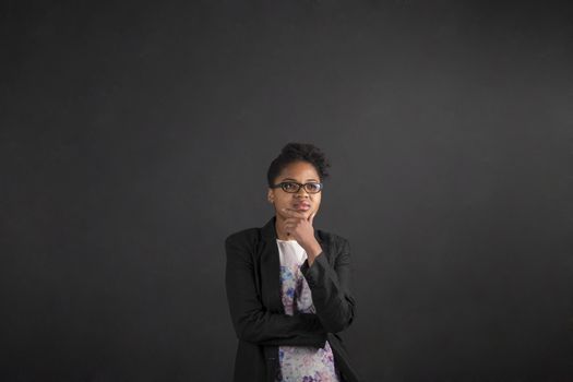 South African or African American black woman teacher or student with her hand on her chin whilst thinking standing against a chalk black board background inside