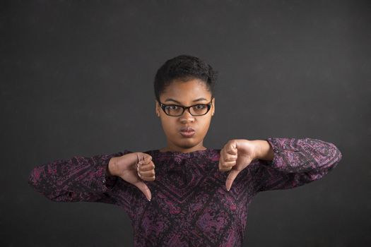 South African or African American black woman teacher or student with thumbs down hand signal on a chalk black board background inside