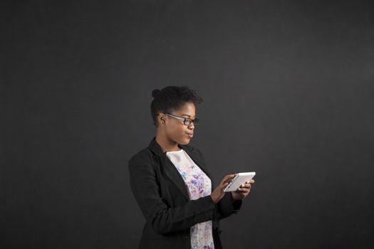 South African or African American black woman teacher or student holding a tablet standing against a chalk blackboard background inside