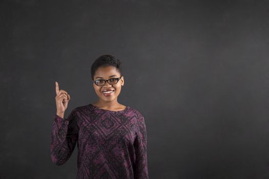 South African or African American black woman teacher or student with a good idea or answer standing against a chalk blackboard background inside