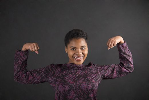 South African or African American black woman teacher or student with strong muscular arms standing against a chalk blackboard background inside