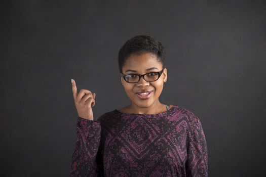 South African or African American black woman teacher or student with a good idea or answer standing against a chalk blackboard background inside