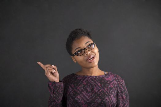 South African or African American black woman teacher or student with a good idea or answer standing against a chalk blackboard background inside