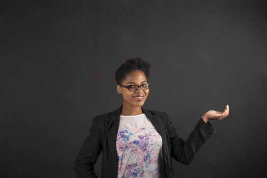 South African or African American black woman teacher or student holding her hand out to the side standing against a chalk blackboard background inside