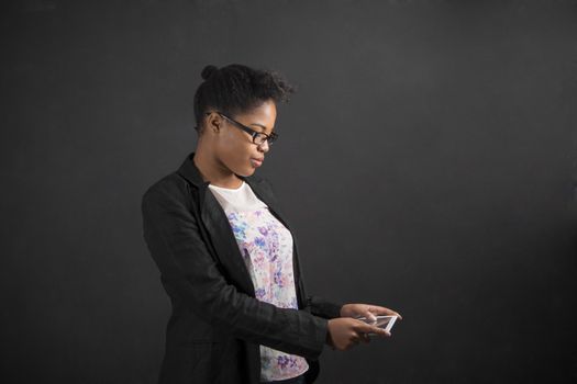 South African or African American black woman teacher or student holding a tablet standing against a chalk blackboard background inside