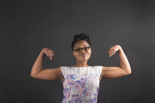 South African or African American black woman teacher or student with strong muscular arms standing against a chalk blackboard background inside