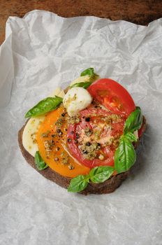 sandwich of rye bread mozzarella, tomato and pesto wrapped in baking paper