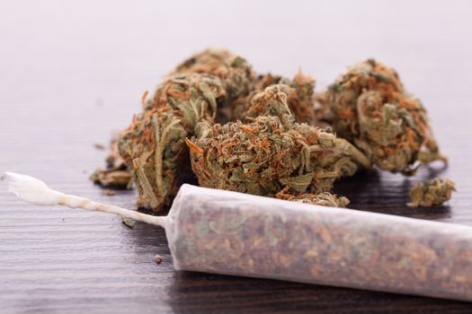 Close up of dried marijuana leaves and tied end of marijuana joint with translucent rolling paper on white background