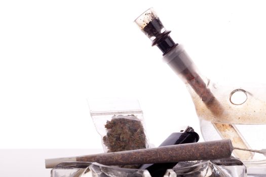 Close up of marijuana joint made with translucent rolling papers, plastic baggy of dried marijuana, black lighter and pipe on white background