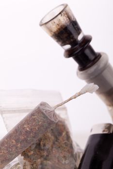 Close up of marijuana joint made with translucent rolling papers, plastic baggy of dried marijuana, black lighter and pipe on white background