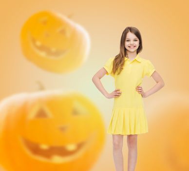 holidays, childhood, happiness and people concept - smiling little girl in dress over halloween pumpkins background