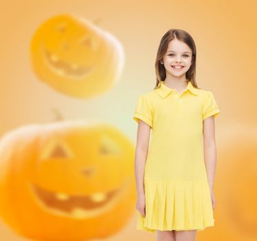 holidays, childhood, happiness and people concept - smiling little girl in dress over halloween pumpkins background