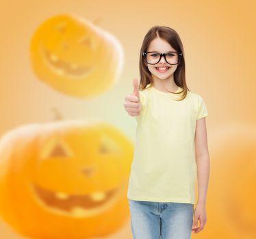 gesture, education, holidays and people concept - smiling little girl in glasses showing thumbs up over halloween pumpkins background