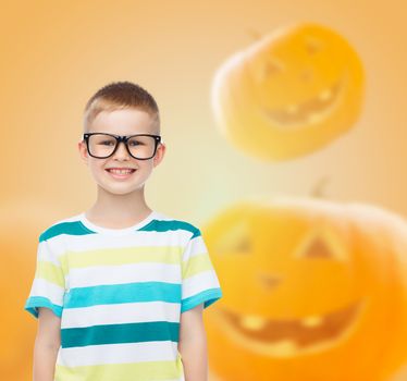 education, holidays, childhood, vision and people concept - smiling little boy in glasses over halloween pumpkins background