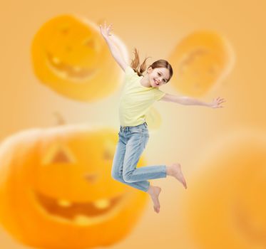 holidays, childhood, happiness and people concept - smiling little girl jumping over halloween pumpkins background