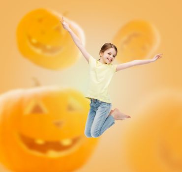 holidays, childhood, happiness and people concept - smiling little girl jumping over halloween pumpkins background